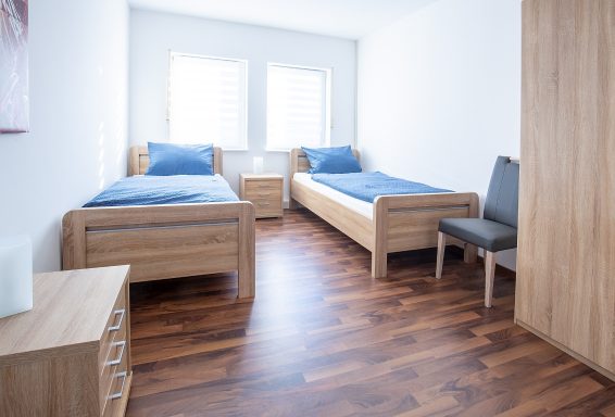 Schlafen 1 Helles Zimmer mit zwei Einzelbetten, Nachttisch und einem Stuhl. Holzfußboden.