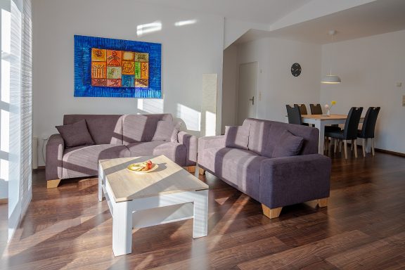 Wohnbereich Helle Wohnraum mit zwei lila Sofas, einem Tisch und einem Esstisch im Hintergrund.