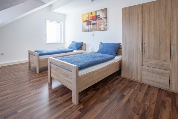 Schlafen 2 Zimmer mit zwei Einzelbetten, Holzfußboden und einem Schrank, hell und modern eingerichtet.