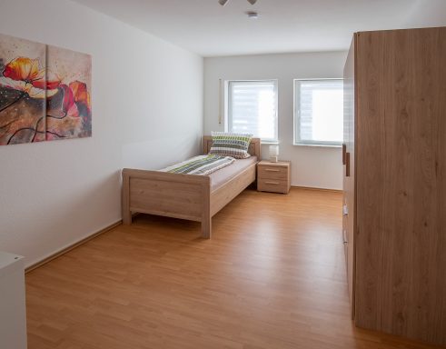 Schlafen 1 Helles, minimalistisches Schlafzimmer mit einem einzelnen Bett und einem Schrank.