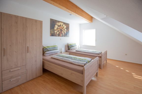 Schlafen 2 Helles Schlafzimmer mit zwei Betten, Holzschrank und modernem Wandbild.